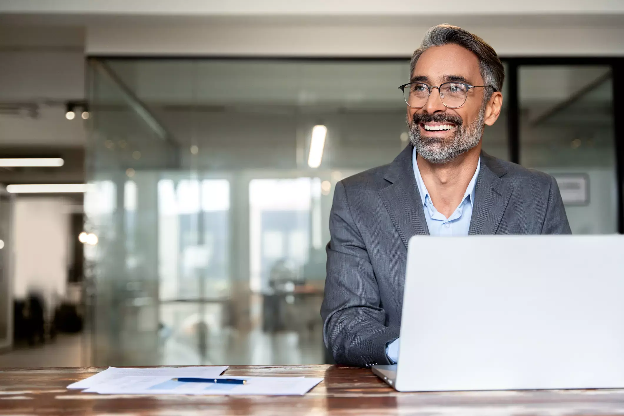 Smiling businessman in a gray suit applying for a business loan on a laptop in a modern office.