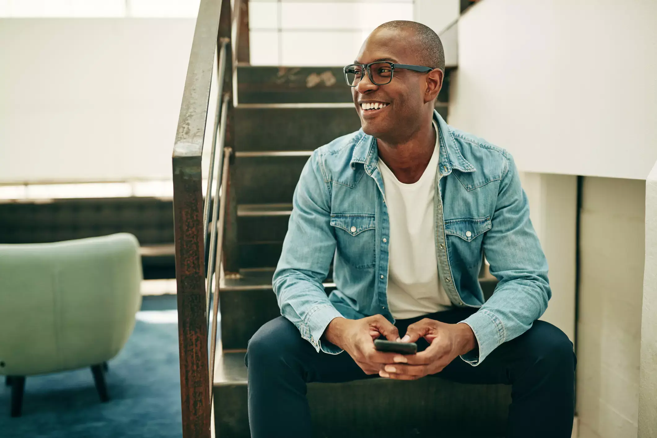 Confident businessman in denim shirt applying for business capital on his smartphone, radiating success and independence